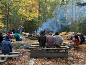 Students gather at campfire circle for morning meeting and one plays the violin