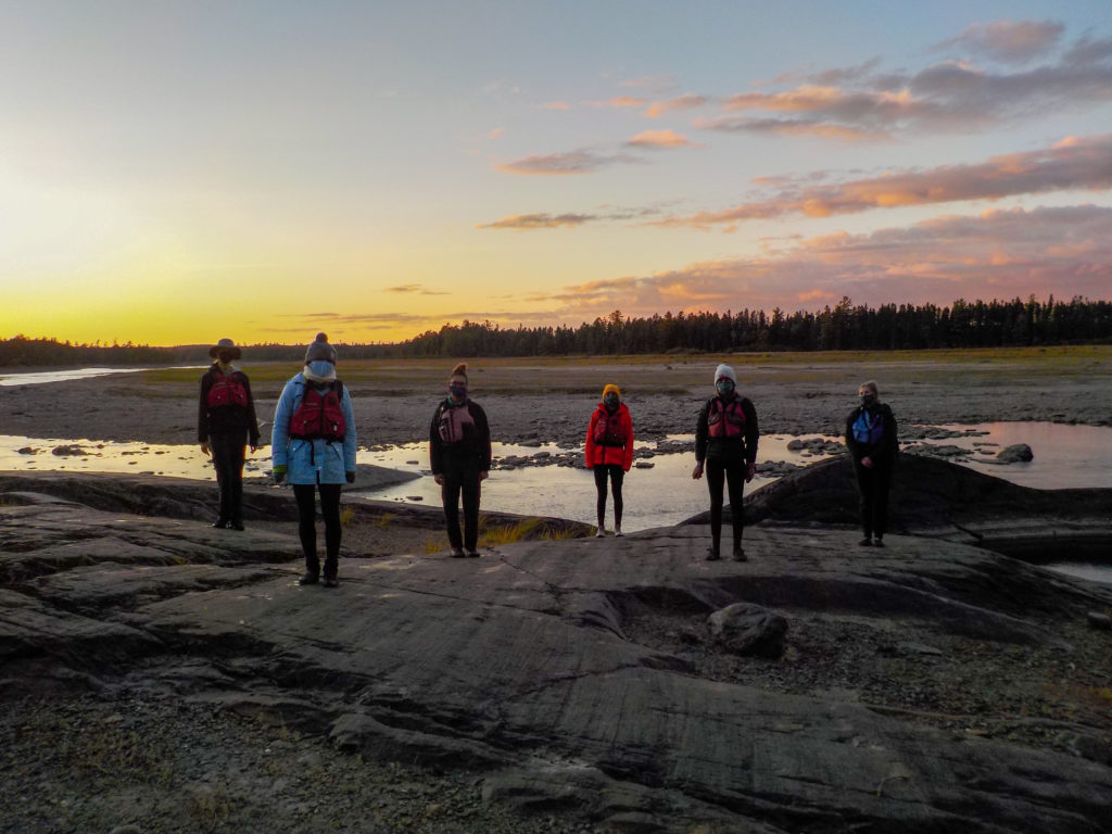 Six students stand facing the camera in front of a beautiful sunset